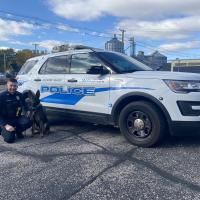 Police officer kneeling next to canine officer with Police car in the background