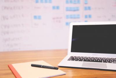 Apple macbook air turned off next to notepad and pen in front of white board